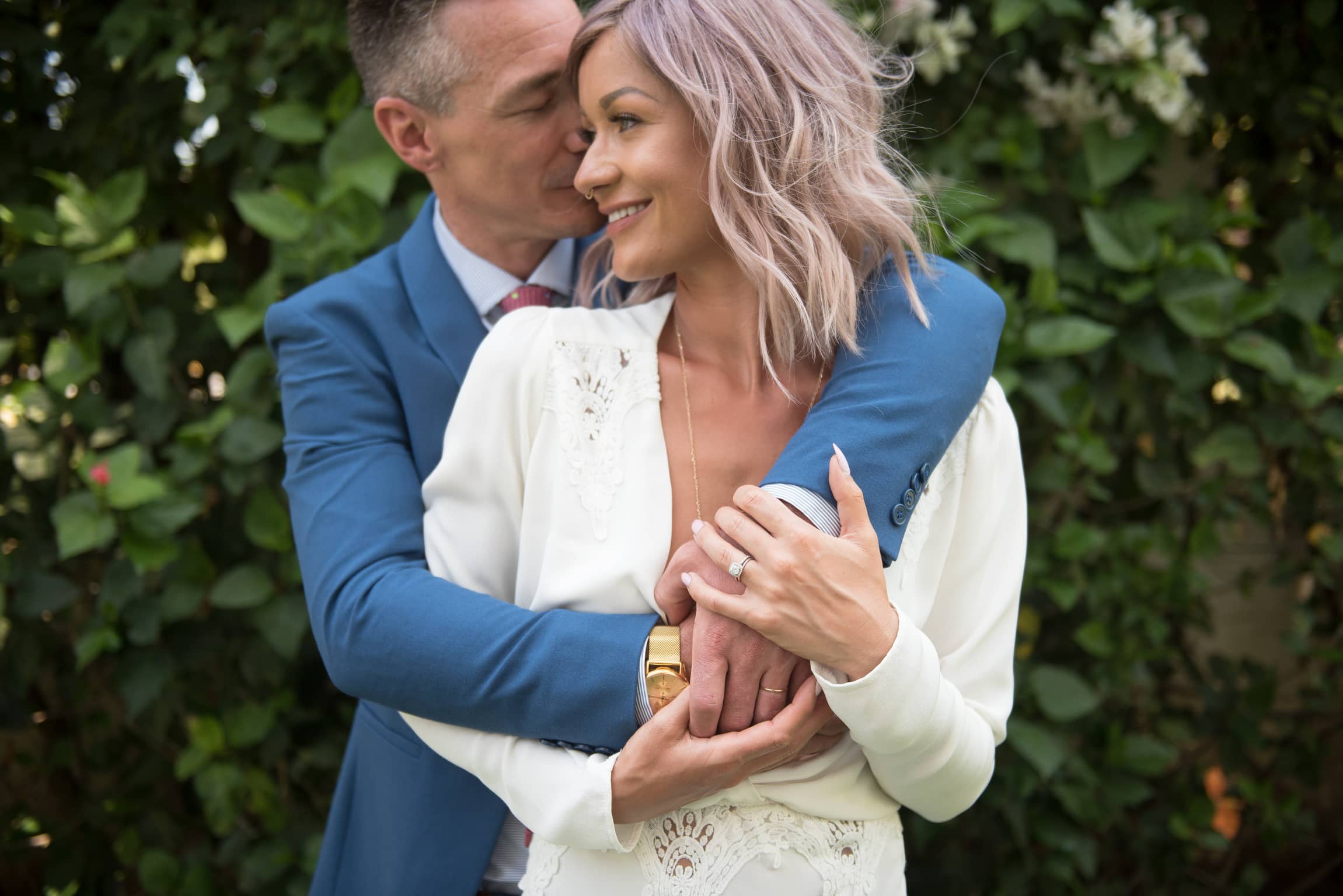 Bride and Groom embracing in front of wall of greenery